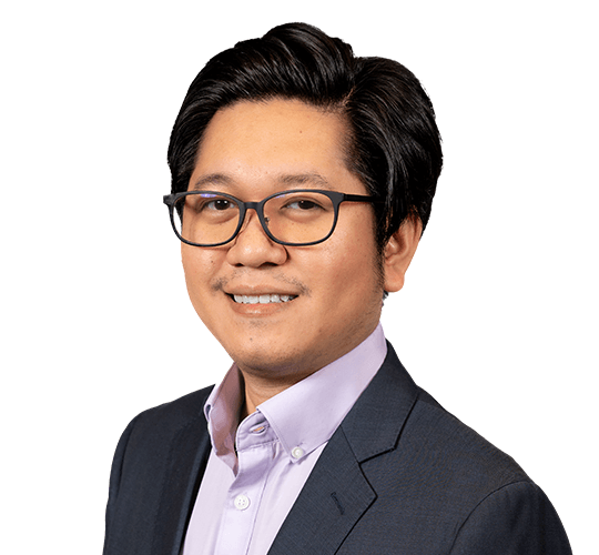 Portrait of a man with glasses in a dark suit and light purple shirt, smiling against a white background.